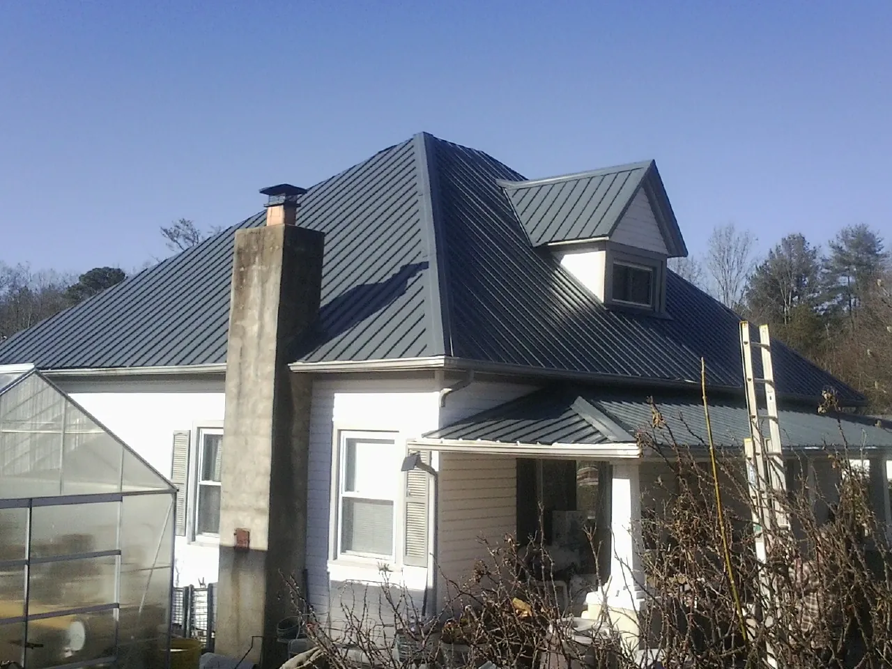 Dark blue standing seam metal roof on a white farmhouse with dormer — Slate & Tile Roof Repair by Roofing Brothers in Mcclusky