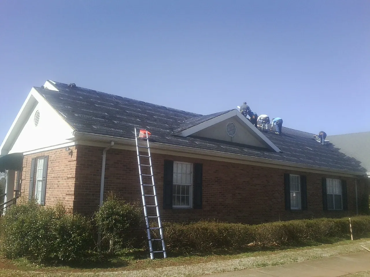 Crew tearing shingles off a brick ranch roof with a ladder set — Emergency Roof Repair work by our crew in Mcclusky