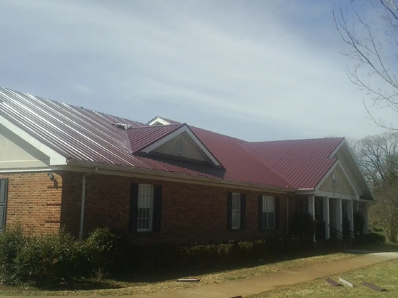 Red metal roof with gabled entries on a long brick building, from a Hail Damage Roof Repair job in Mcclusky