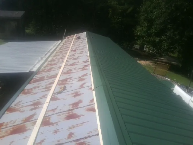 Old rusted panels beside newly installed green metal roofing — Wind Damage Roof Repair by Roofing Brothers in Mcclusky