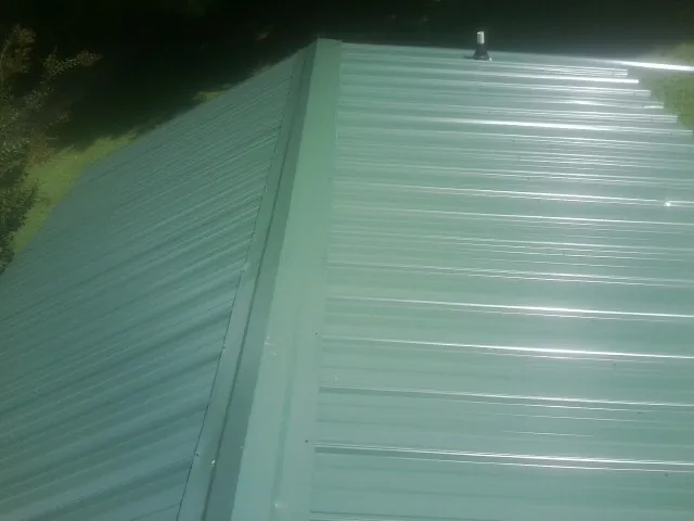 New green metal panels meeting at the ridge of a roof — Flat Roof Repair work by our crew in Mcclusky
