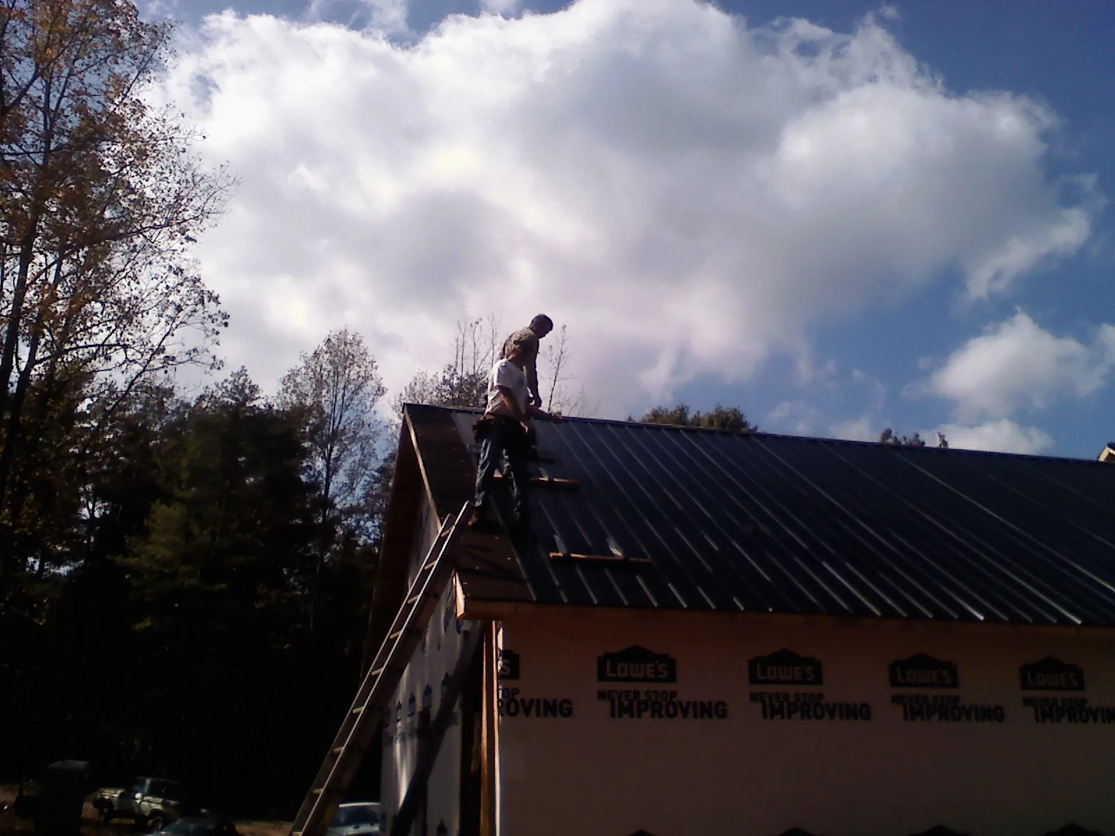 Roofer fastening dark metal panels high against a cloudy sky, from a Roof Inspection job in Mcclusky