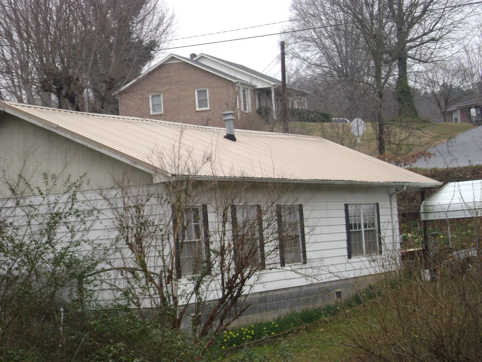 Tan metal roof on a white sided house set into a hillside — Commercial Roofing by Roofing Brothers in Mcclusky