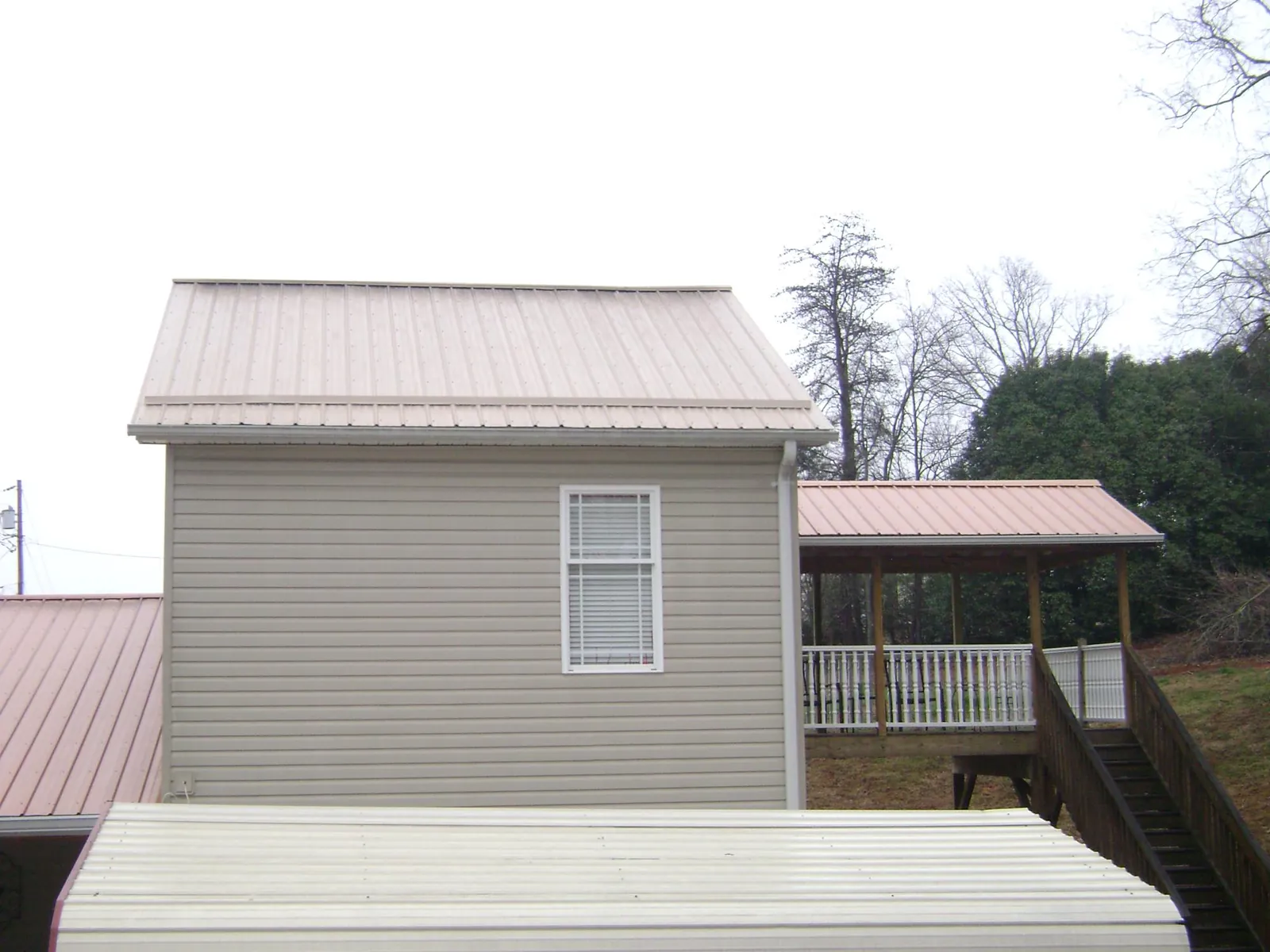 Tan metal roofs on a two story addition and attached porch, from a Roof Replacement job in Mcclusky